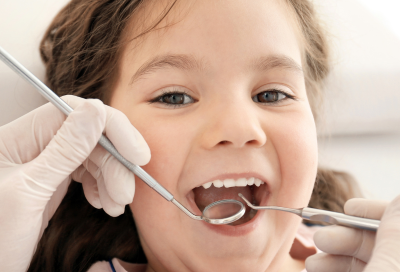 Little girl smiling while getting her teeth worked on at the dentist, representing how to prepare your child for the dentist