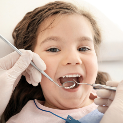 Little girl smiling while getting her teeth worked on at the dentist, representing how to prepare your child for the dentist