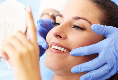 Woman looking at her teeth in a small mirror at the dentist, representing comprehensive same-day dental services