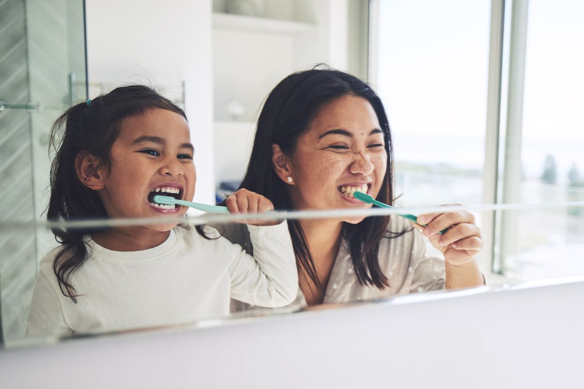 Expert-dental-care-near-brook-valley-brushing-teeth Happy mother and daughter brushing teeth together in morning routine by bathroom mirror, highlighting expert dental hygiene, oral care, and tooth whitening near brook valley.