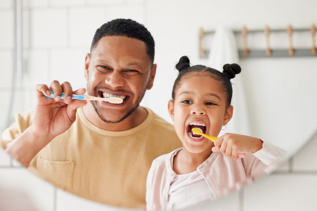 Father and child brushing teeth together in bathroom mirror
