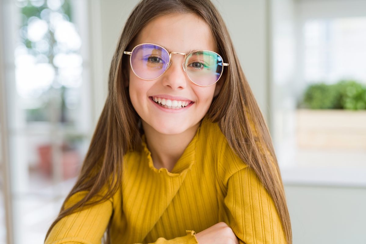 Expert-pediatric-dental-checkups-north-carolina Young girl with glasses smiling and looking away thoughtfully