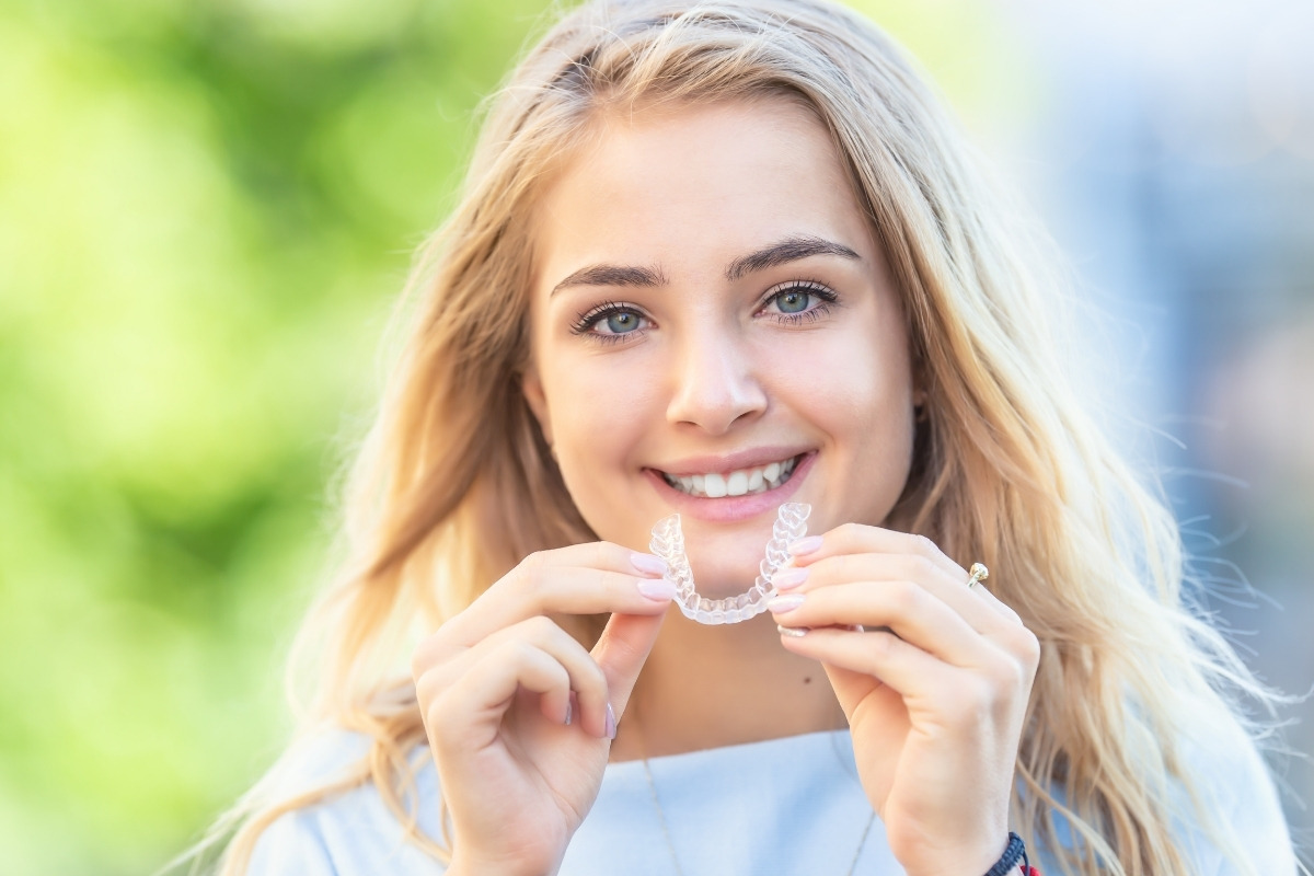 The-dental-care-center-invisalign Smiling woman holding clear invisalign aligners, showcasing discreet orthodontic treatment at the dental care center.
