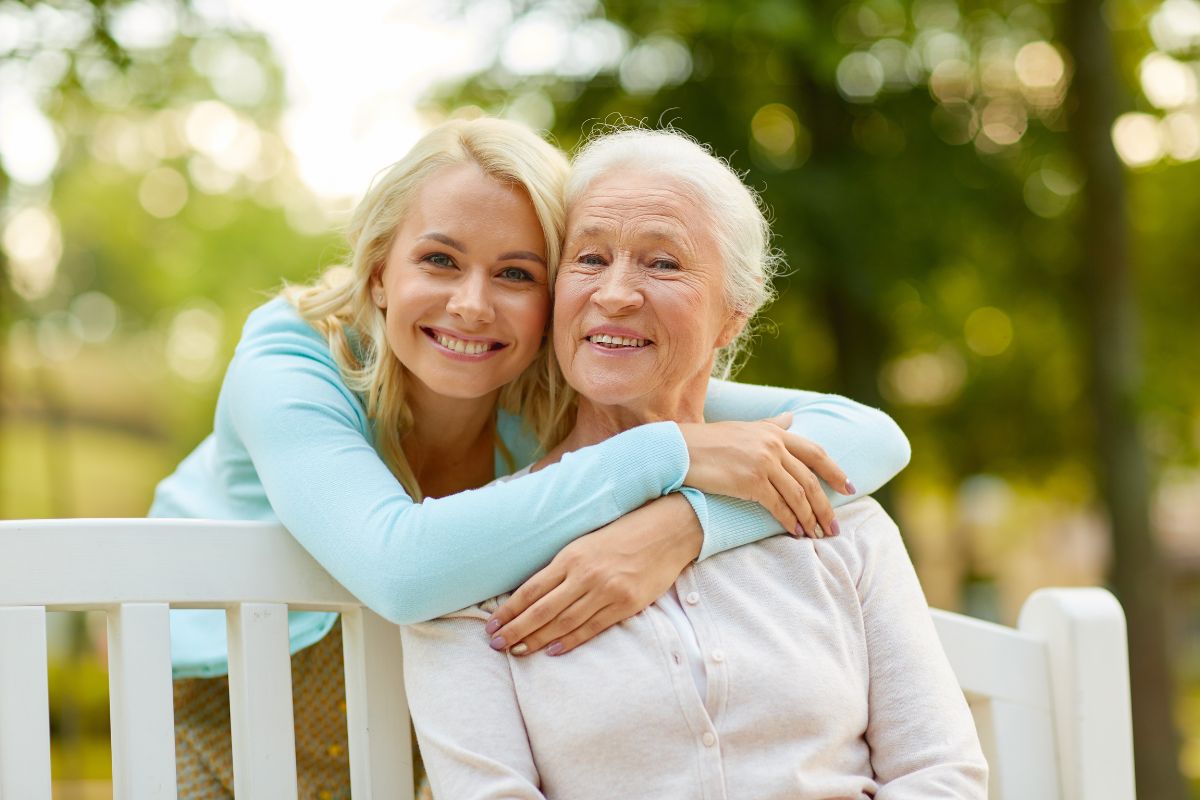 Top-rated-comprehensive-dental-care-elm-city Happy young daughter hugging senior mother on park bench, representing family, generations, and dental care services including same-day dentures, restorative and cosmetic dentistry near elm city.