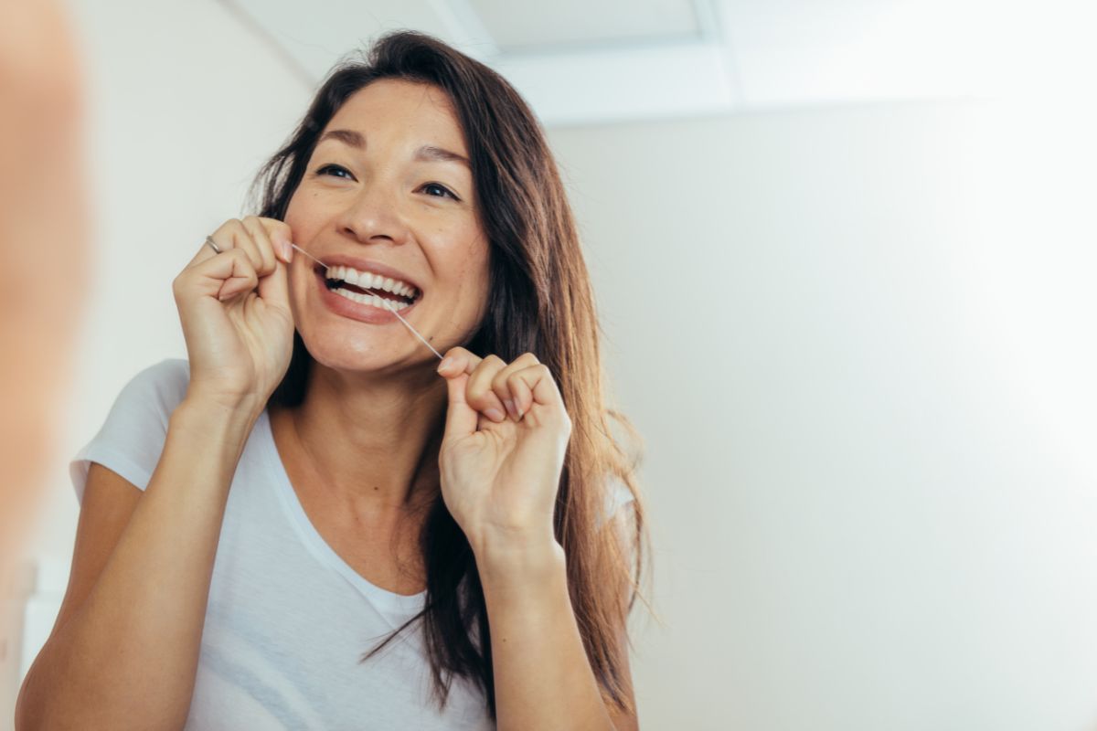 Woman using dental floss in bathroom mirror