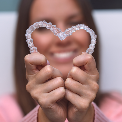 Benefits of invisalign over traditional braces 4 Woman holding two invisalign aligners together in the shape of a heart, representing benefits of invisalign over traditional braces