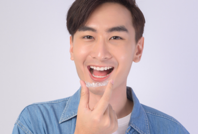 Man smiling while holding invisalign aligners up to his mouth, representing faqs about invisalign