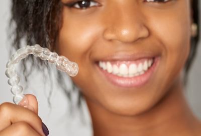 Teenage girl smiling and holding invisalign aligner, representing what is invisalign?